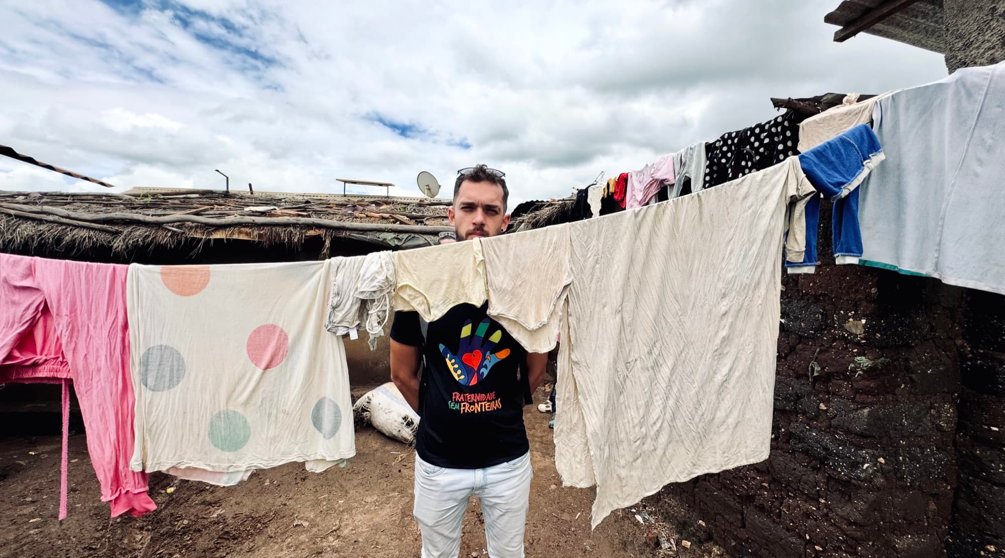 Felipe entre varais de roupa, com a camiseta da Fraternidade sem Fronteiras